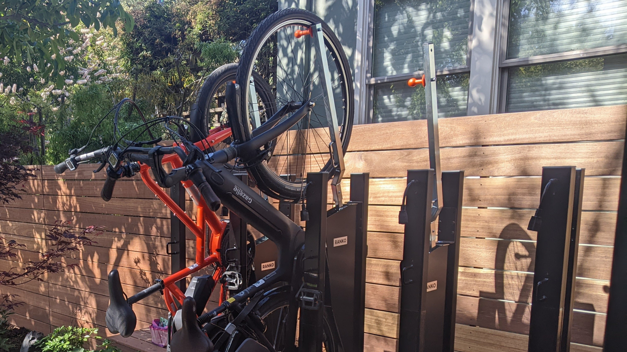 Bicycle rack with multiple bikes attached outdoors against a wooden fence.